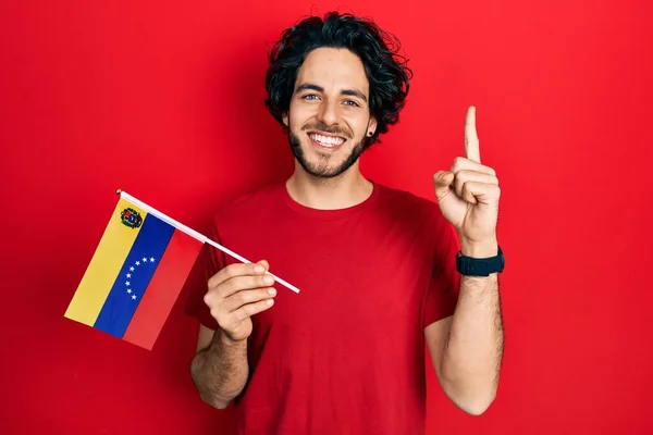 ハンサムなヒスパニック系の男を保持Venezuelanフラグ笑顔でアイデアや質問を指差す指で幸せな顔 ナンバーワン — ストック写真