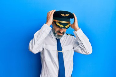 Sakallı, gri saçlı, uçak pilotu üniforması giyen baş ağrısı çeken, çaresiz ve stresli bir orta yaşlı adam. Ağrı ve migren yüzünden. Eller başının üstünde.. 