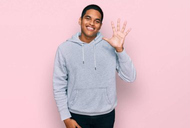 Genç, yakışıklı, sıradan bir kazak giyen, beş numaralı parmaklarını göstererek gülümseyen, kendinden emin ve mutlu bir İspanyol.. 