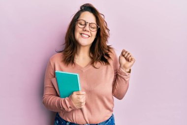 Genç beyaz kadın elinde kitapla gururla bağırıyor zaferi ve başarıyı kutluyor. 