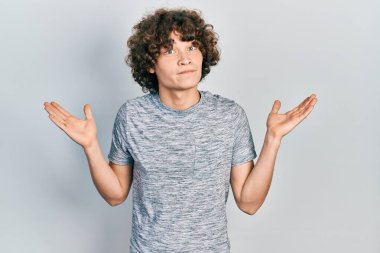 Gri bir tişört giyen yakışıklı genç adam, hiçbir şeyden habersiz ve kolları açık, hiçbir fikri yok ve şüpheli bir yüzü var.. 