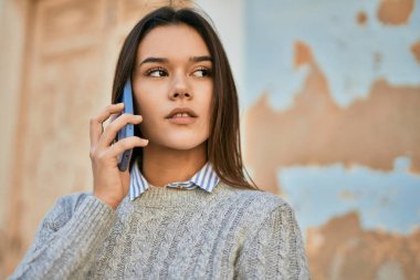 Ciddi bir suratı olan genç İspanyol kız şehirde akıllı telefondan konuşuyor..