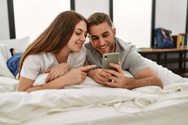 Kafkasyalı genç bir çift evde yatarken akıllı telefon kullanıyor..