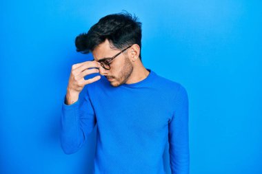 Gündelik kıyafetler ve gözlük takan genç İspanyol adam yorgun burnu ve gözleri ovuşturup yorgunluk ve baş ağrısı hissediyor. Stres ve hüsran kavramı. 