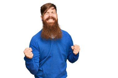 Genç İrlandalı kızıl elbiseli mutlu ve heyecanlı bir adam kolları havada, gülümseyen ve başarı için çığlık atan kazanan bir jest yapıyor. kutlama konsepti. 