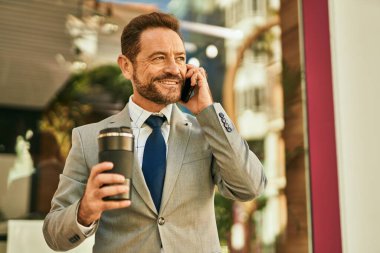 Orta yaşlı işadamı akıllı telefondan konuşuyor ve şehirde kahve içiyor..