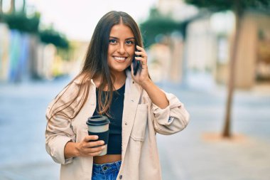 Genç İspanyol kız gülümsüyor. Akıllı telefonla konuşuyor ve şehirde kahve içiyor..