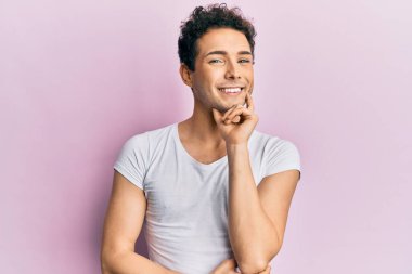 Gündelik beyaz tişört giyen genç yakışıklı kameraya kendinden emin kollarını kavuşturmuş ve çenesini kaldırmış bir şekilde bakıyor. Olumlu düşünmek. 