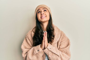 Yün kazak ve kış şapkası giyen genç İspanyol kadın elleri ile yalvarıyor ve dua ediyor. Yüzünde umut ifadesi var. Çok duygusal ve endişeli. Yalvarıyor. 