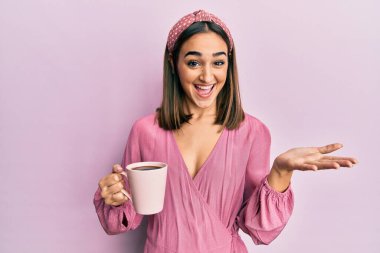 Genç esmer kız bir fincan kahve içerek başarıyı mutlu bir gülümsemeyle ve kazanan yüz ifadesiyle kutluyor. 