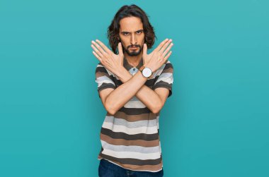 Gündelik kıyafetler giyen genç İspanyol adam. Reddedilmiş yüz ifadesi. Kollarını kavuşturup negatif işaret veriyor. 