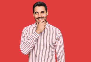 İş gömleği giyen genç İspanyol adam kameraya kendinden emin bakıyor kollarını kavuşturup gülümsüyor ve çenesini kaldırıyor. Olumlu düşünmek. 