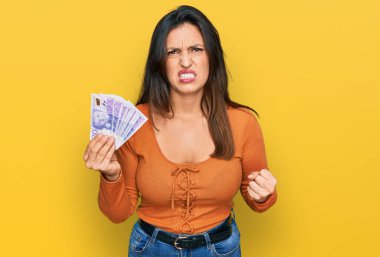 Güzel İspanyol kadın elinde 20 İsveç banknotuyla sinirlenmiş ve sinirlenmiş bir şekilde bağırıyor, öfkeden deliler gibi bağırıyor ve el kaldırıyor. 