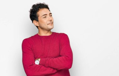 Sıradan kıyafetler giyen genç yakışıklı kolları çaprazlanmış ve kendinden emin bir şekilde yan tarafa bakıyor. 