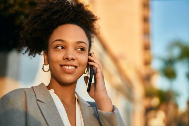 Genç afro-amerikan iş kadını gülümseyerek şehirdeki akıllı telefondan konuşuyor..