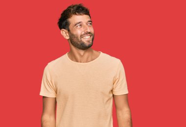 Sakallı, sıradan tişörtlü, yüzünde gülümseme ve doğal ifadeyle yan yana bakan yakışıklı bir genç. Kendinden emin gülen. 