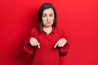 Orta yaşlı İspanyol kadın, gündelik giysiler içinde üzgün ve üzgün görünüyor, parmaklarıyla yön gösteriyor, mutsuz ve depresif.. 