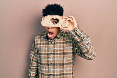 Genç Afrikalı Amerikalı adam elinde kalp şeklinde ekmek tutuyor. Şaşırmış ve şaşırmış bir ifade, korku ve heyecanlı bir yüz ifadesi var.. 