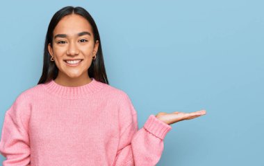 Genç Asyalı kadın, günlük kışlık süveter giyip neşeli bir şekilde sunum yapıyor ve avuç içi kameraya bakıyor.. 