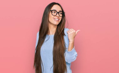 Gündelik kıyafetler ve gözlük takan neşeli yüzüyle gülümseyen ve baş parmağıyla yüzünü gösteren İspanyol genç kız.. 