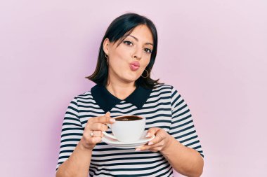 Genç İspanyol kadın bir fincan kahve içiyor ve kameraya bakıp öpüşürken sevimli ve seksi oluyor. aşk ifadesi. 