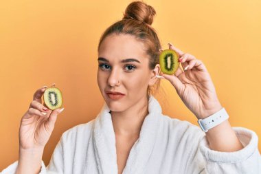 Bornoz giyen genç sarışın kadın elinde taze kivi tutarken yüzünde ciddi bir ifadeyle rahatladı. Basit ve doğal bir şekilde kameraya bakıyorsun.. 