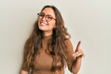 Gündelik kıyafetler giyen ve gözlüklü genç İspanyol kız bir numarayı gösterip işaret ederken kendinden emin ve mutlu bir şekilde gülümsüyor.. 