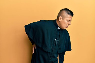 Sarı arka planda dikilen genç Latin rahip sırt ağrısı çekiyor, elleriyle dokunuyor, kas ağrısı çekiyor. 