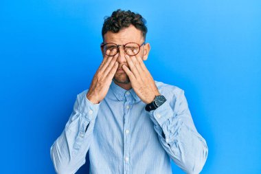 Günlük kıyafetler giyen ve gözlük takan genç İspanyol adam yorgunluk ve baş ağrısı için gözlerini ovuşturuyor, uykulu ve yorgun bir ifade takınıyor. görme sorunu 