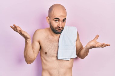 Tişörtsüz ve kafası karışık genç kel bir adam kolları açık, hiçbir fikri yok ve şüpheli bir yüzü var.. 