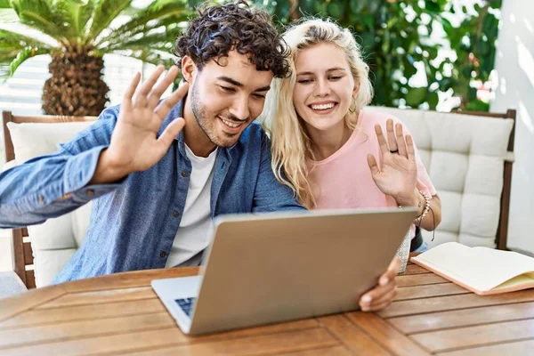 一对年轻夫妇笑着高兴地坐在阳台的桌子上 用笔记本电脑打了一个视频电话 — 图库照片