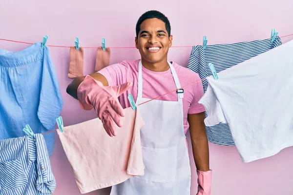 Joven Hombre Hispano Guapo Usando Delantal Más Limpio Sosteniendo Ropa —  Fotos de Stock