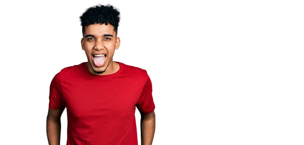 カジュアルな赤いTシャツを着た若いアフリカ系アメリカ人男性が面白い表情で幸せ舌を突き出しています 感情の概念 — ストック写真