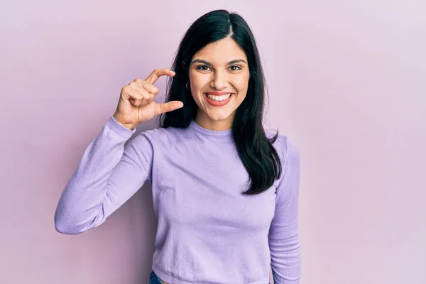 カジュアルな服を着た若いヒスパニック系の女性が笑顔で 指を見てカメラで小さなサイズの看板を行う手で自信を持ってジェスチャー 概念を測定し — ストック写真