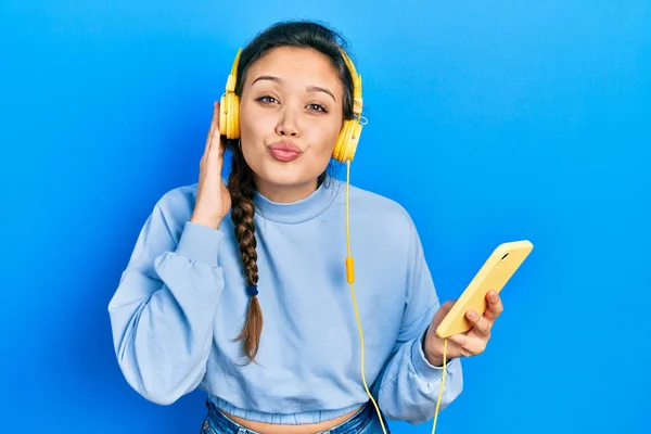 Ung Latinamerikansk Tjej Med Smartphone Och Hörlurar Tittar Kameran Blåser — Stockfoto