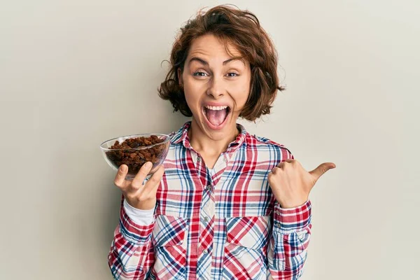 Young Brunette Woman Holding Bowl Raisins Pointing Thumb Side Smiling — Stock Photo, Image
