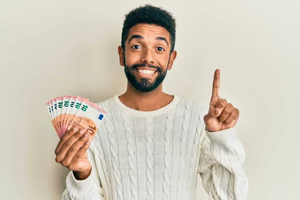10ユーロ紙幣の束を保持ひげを持つハンサムなヒスパニック系の男幸せな顔で指を指すアイデアや質問で笑顔 ナンバーワン — ストック写真