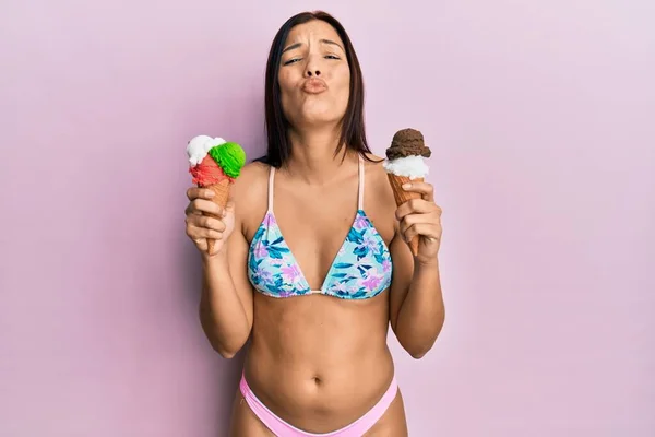 ビキニを着た若いラテン系の女性がカメラを見てアイスクリームを持っていて キスが可愛くてセクシーさを吹いています 愛の表現 — ストック写真