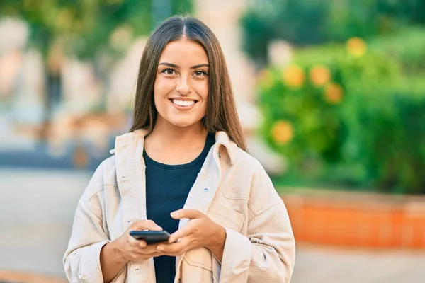 若いですヒスパニック系の女の子笑顔幸せな使用してスマートフォンで公園 — ストック写真