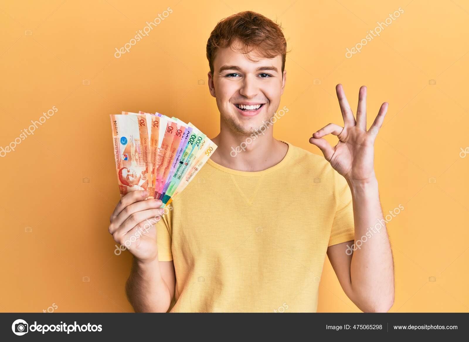 年轻的高加索人手里拿着菲律宾比索钞票手拿着手签微笑着友好的手势表示出极好的象征——图库图片© Krakenimages.com #475065298