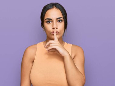 Genç esmer kadın gündelik kıyafetler giyip parmakları dudaklarında sessiz olmak istiyor. sessizlik ve gizli konsept. 