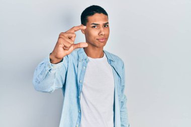 Genç Afro-Amerikalı, günlük kıyafetler giymiş, gülümseyen, kendine güvenen, el hareketi yapan, parmaklarıyla işaret yapan ve kameraya bakan bir adam. ölçüm kavramı. 