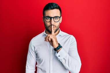 Genç İspanyol iş adamı gömlek ve gözlük takıyor ve parmakları dudaklarında sessiz olmak istiyor. sessizlik ve gizli konsept. 