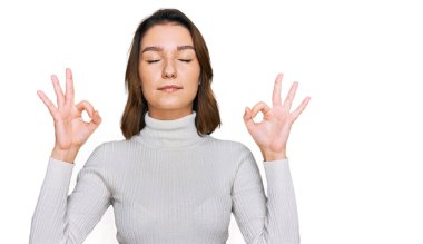 Rahat kıyafetler giyen, gözleri kapalı gülümseyen genç beyaz kız parmaklarıyla meditasyon hareketi yapıyor. yoga konsepti. 