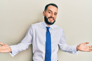 Sakallı, iş kravatlı, kafası karışmış, elleri ve kolları havada genç bir adam. şüphe kavramı. 