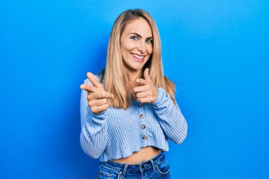 Gündelik giysiler giymiş genç beyaz kadın mutlu ve komik yüzüyle kamerayı işaret ediyor. iyi enerji ve titreşimler. 