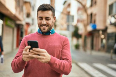 Genç İspanyol adam şehirde akıllı telefon kullanarak mutlu gülümsüyor..