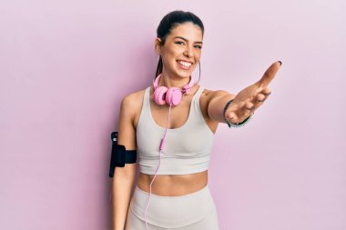 Spor kıyafetleri giyen, kulaklık takan, gülümseyen, dostça el sıkışan genç İspanyol bir kadın. başarılı iş. 