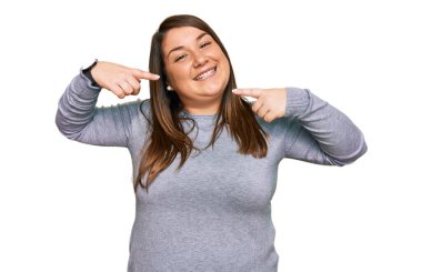 Güzel esmer, iri yarı, günlük kıyafetler giyen neşeli gülümseyen, parmaklarıyla ve ağzıyla işaret eden bir kadın. diş sağlığı kavramı. 