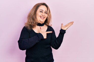 Orta yaşlı beyaz kadın, sıradan kıyafetler giyip kameraya hayret ediyor ve gülümsüyor.. 